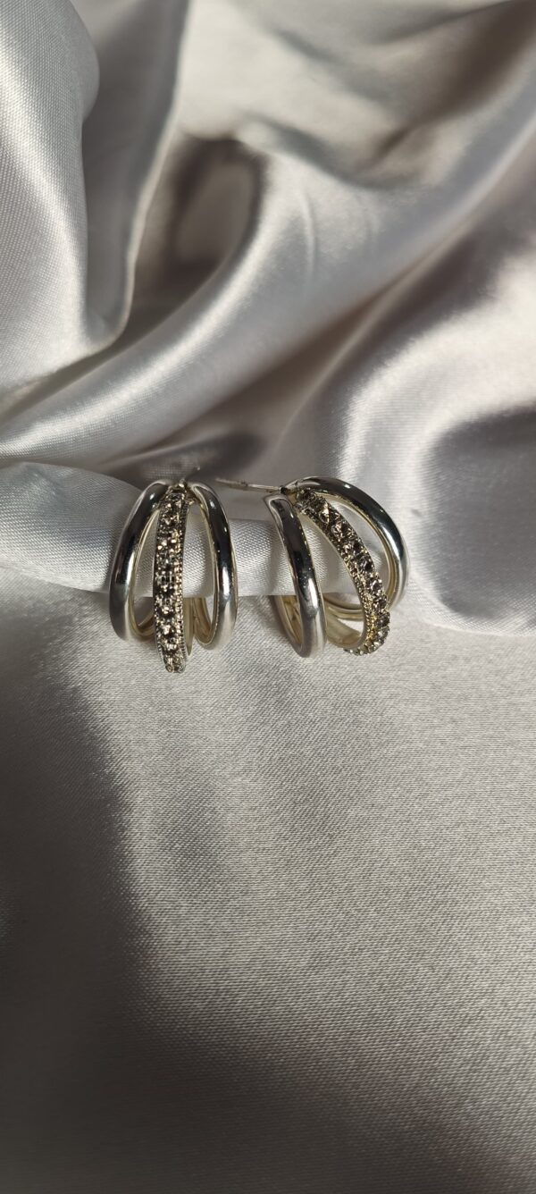 Elegant silver triple hoop earrings with crystal detailing on satin background"